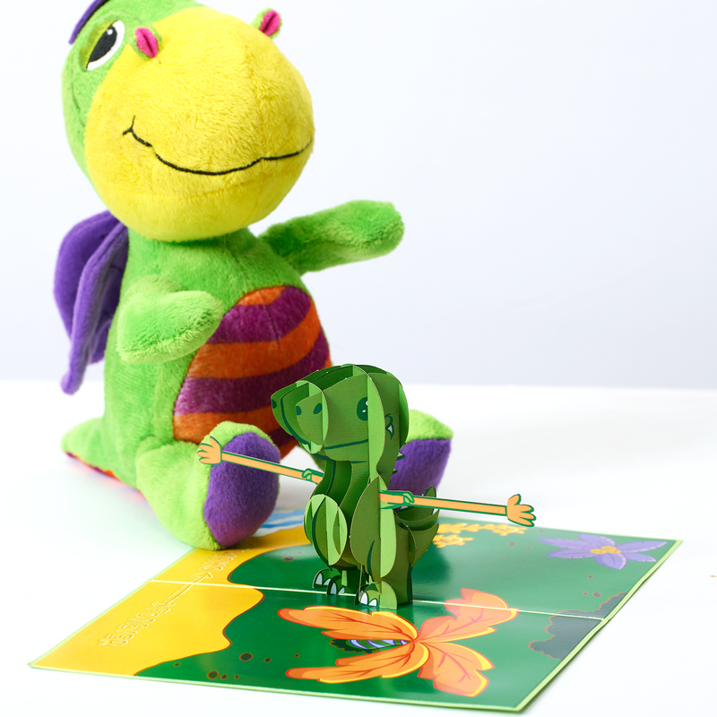 A green dinosaur on a green board, accompanied by a butterfly. A lovely valentine's day card featuring a pop-up T-rex with extended arms, and the words 'always and forever' written in sand on the beach.