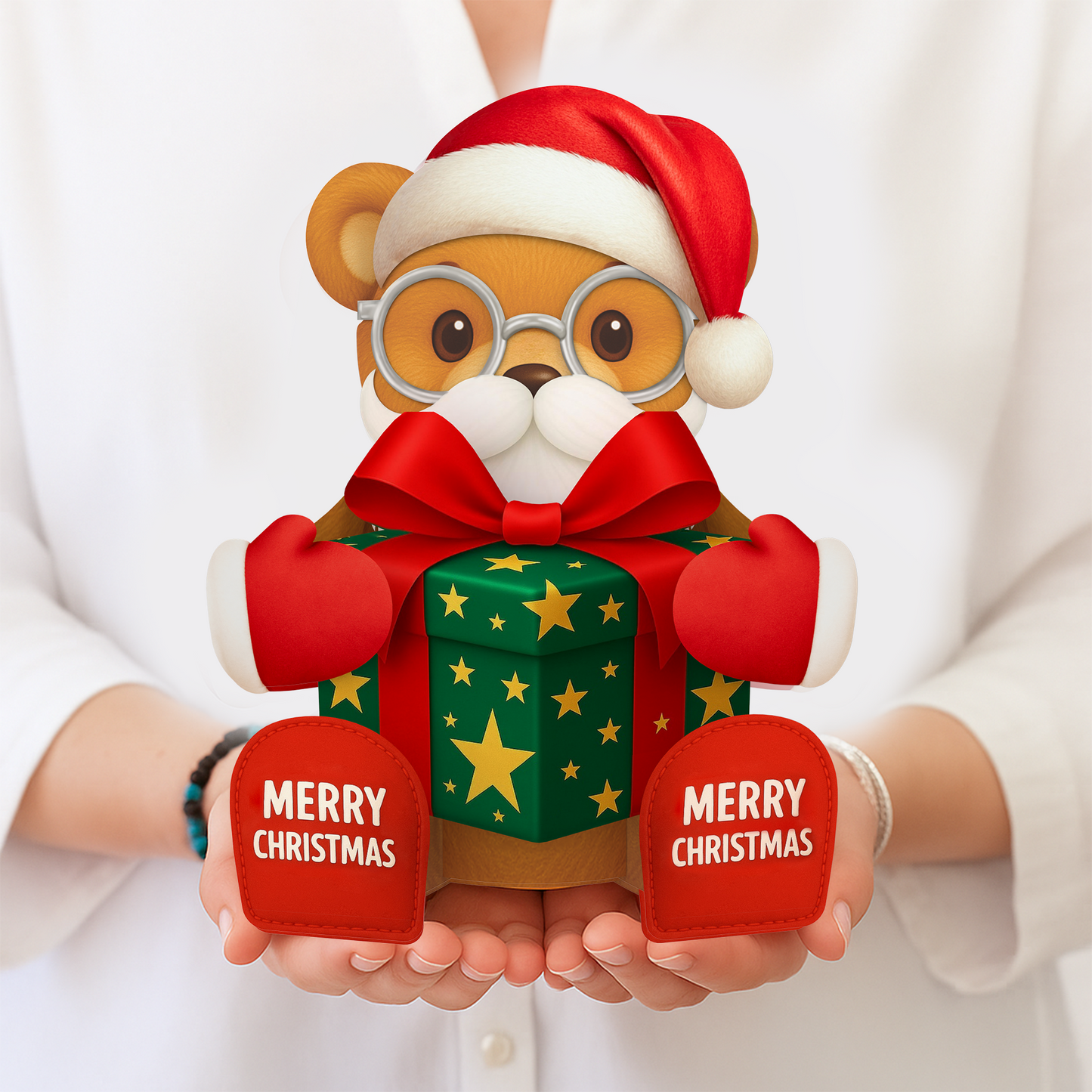 Teddy bear wearing a Santa hat and holding a gift box with 'Merry Christmas' tags, held by a person.