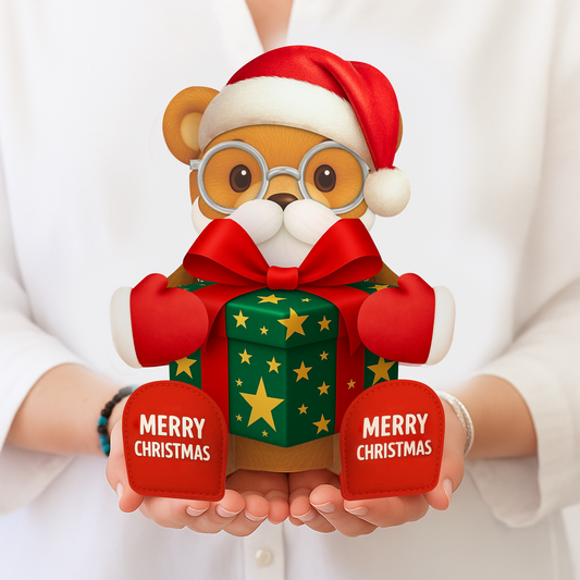 Teddy bear wearing a Santa hat and holding a gift box with 'Merry Christmas' tags, held by a person.