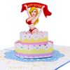 A pop-up card featuring a beautiful woman standing on top of a cake, celebrating joyfully holding a banner that reads, Happy Birthday