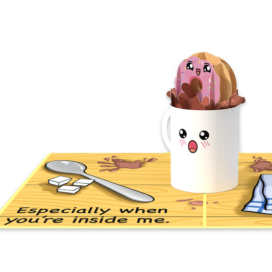  A cup with a donut inside, a spoon on a table. A humorous anniversary pop-up greeting card of a donut being dipped in coffee.