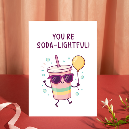 Whimsical birthday card with an adorable soda cup character holding a balloon and waving happily. The bright pastel colors and soda pun message give this card a lively, celebratory feel.