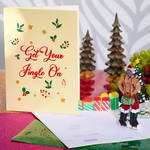 A jolly Santa in a red suit poses beside a festive Christmas tree, holding two huge ornaments. Perfect for a funny holiday card!