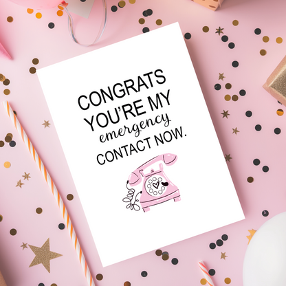 A minimalist greeting card featuring the phrase “Congrats you’re my emergency contact now” in bold black lettering with a pink vintage telephone illustration below. The clean white background and playful design make it perfect for modern relationships, anniversaries, or Valentine’s Day gifts for couples.