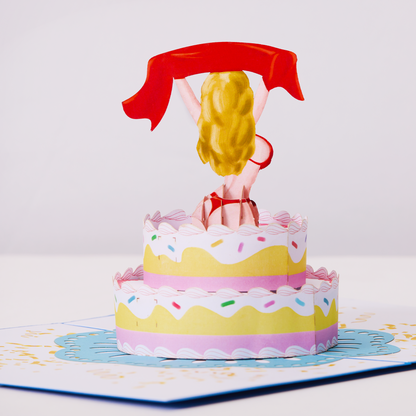 A beautiful woman standing on a cake in a pop-up card.