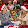 Two children wearing Santa hats holding a reindeer toy with a family in the background.