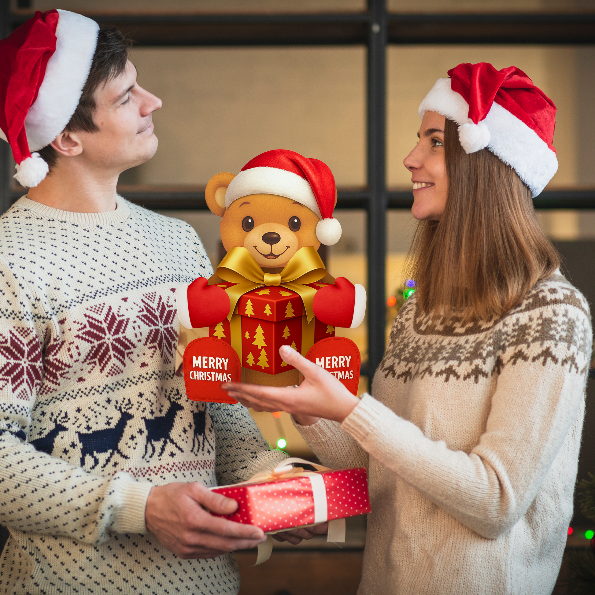 Two people wearing Santa hats holding a Christmas-themed teddy bear and gift box.
