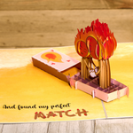 A pop-up card with a fiery background and a couple kissing. Online dating card with two matchsticks who have found their perfect match.