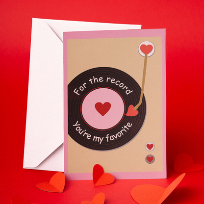 A romantic greeting card with a vinyl record design and the message "For the record, you're my favorite." The card is placed against a red background, accompanied by a white envelope and scattered heart-shaped decorations, creating a warm and heartfelt atmosphere.