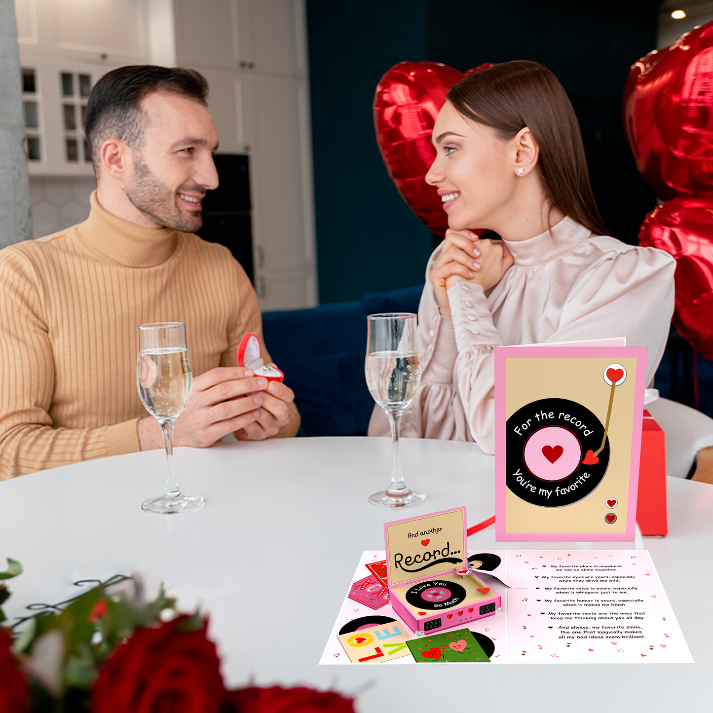 A romantic scene with a couple at a table, where the man is proposing. A vinyl record-themed 3D pop-up card is displayed, featuring the message "For the record, you're my favorite." Red heart-shaped balloons and champagne glasses add to the intimate atmosphere.