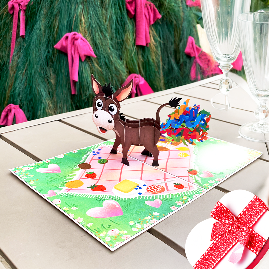 3D pop-up card featuring a surprised donkey with colorful confetti, set on a picnic-themed background.