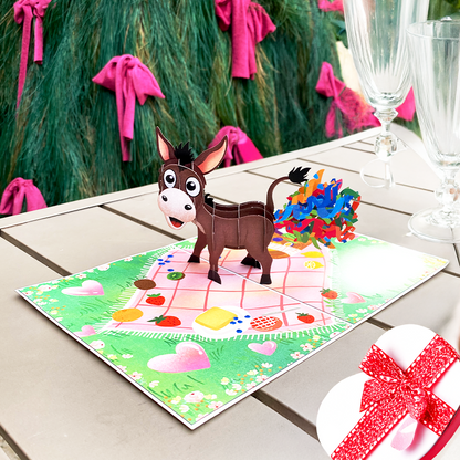 3D pop-up card featuring a surprised donkey with colorful confetti, set on a picnic-themed background.
