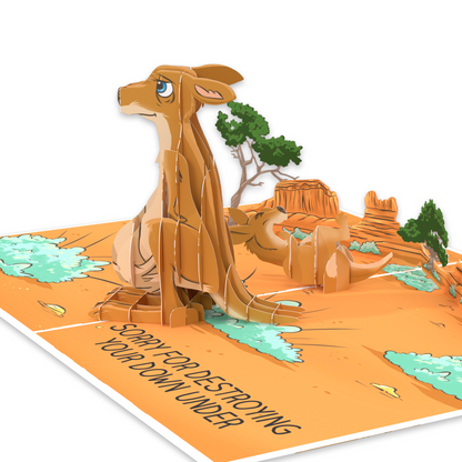 A pop-up card featuring a 3D kangaroo looking sad, set in a desert landscape with trees and rock formations. The text reads, Sorry for destroying your Down Under, adding a humorous touch to the scene.