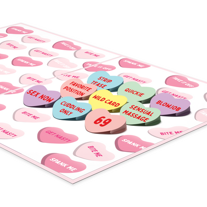 An open greeting card with a playful design featuring colorful candy hearts with cheeky phrases like Strip Tease, Quickie, Wild Card, and 69. The card's background is filled with similar flirty message