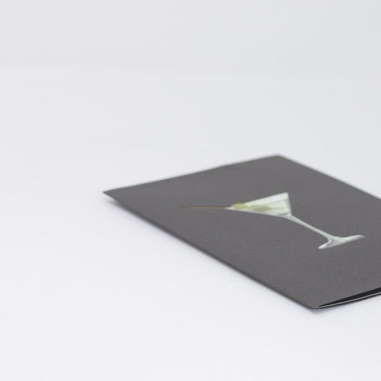 A video shows a pop-up card opening to reveal a 3D woman lounging in a martini glass, playfully holding a stirrer. The cover features a martini with olives, creating a fun and celebratory scene.