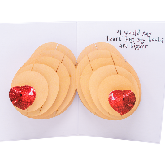 Inside of a humorous pop-up greeting card showing a 3D pair of breasts with red sequin hearts as nipples. The message *I would say heart but my boobs are bigger is written on the right side