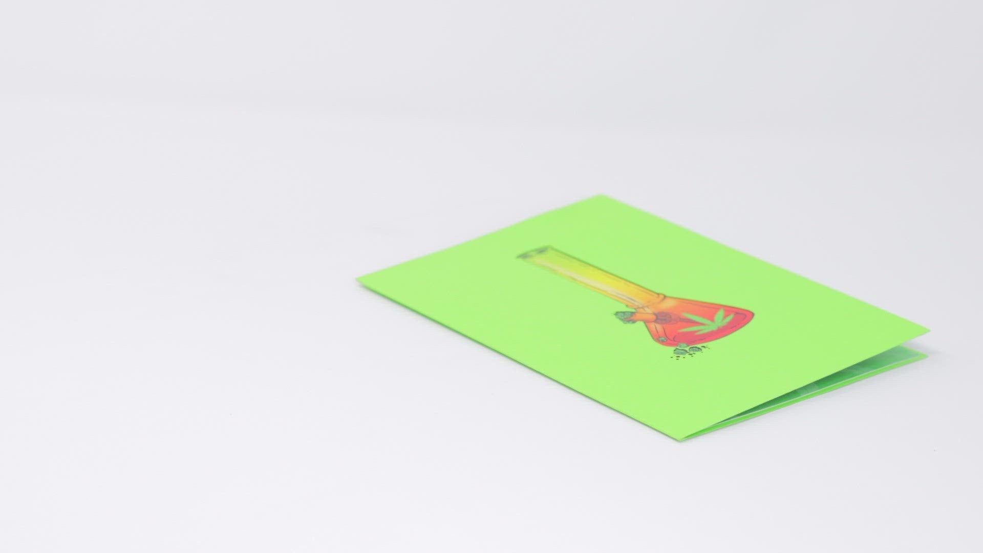 A video shows a pop-up card with a 3D bong design being opened and displayed. The camera pans around to capture the colorful details of the bong illustration, while a real bong and lighter are placed nearby, enhancing the playful theme.