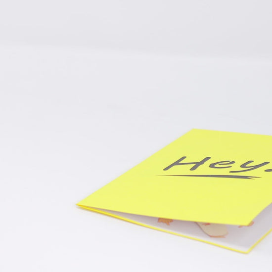 A video shows a pop-up card opening to reveal a 3D hand giving the middle finger. The cover features the word Hey! in bold black on a bright yellow background, adding a playful and cheeky surprise.